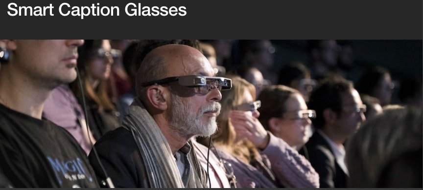 A imagem mostra um grupo de pessoas a utilizar óculos inteligentes de legendas durante um espetáculo. 